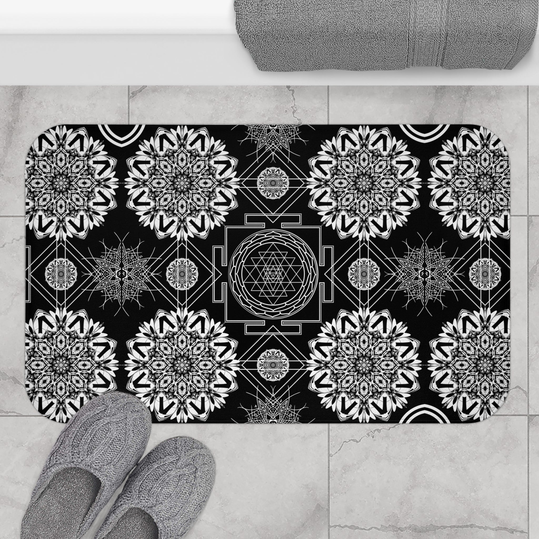 Mystical bath mat with a central Sri Yantra sacred geometry diagram surrounded by intricate white mandala snowflakes and geometric linework on deep black displayed on marble tile flooring