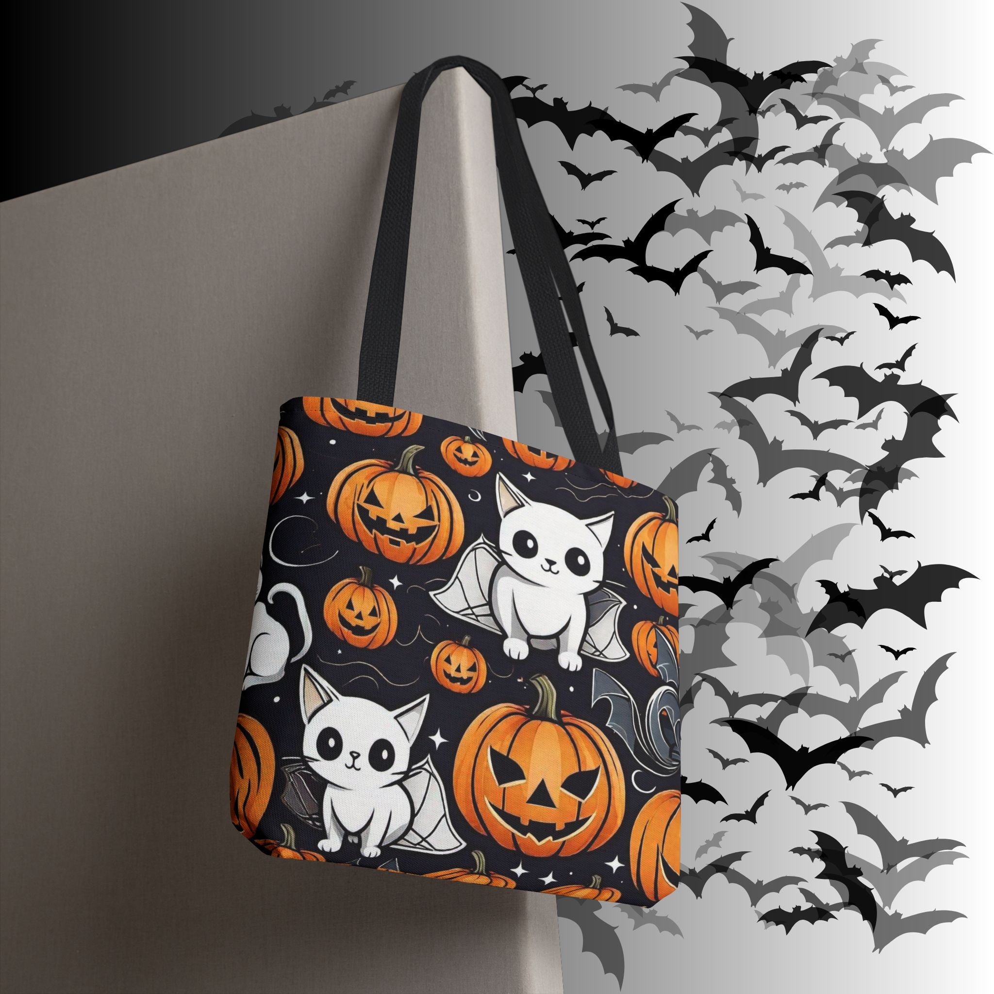 Black polyester tote bag with repeating pattern of wide-eyed white bat kittens and glowing orange jack-o'-lanterns with star sparkle accents