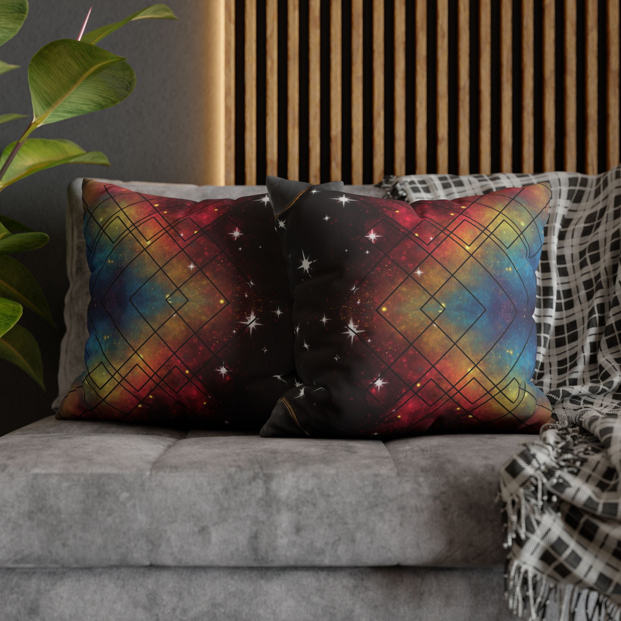 Two square throw pillows on a grey sofa featuring a vivid nebula in deep red, electric blue, and gold overlaid with a repeating geometric diamond grid in fine black linework with white starburst sparkles scattered throughout