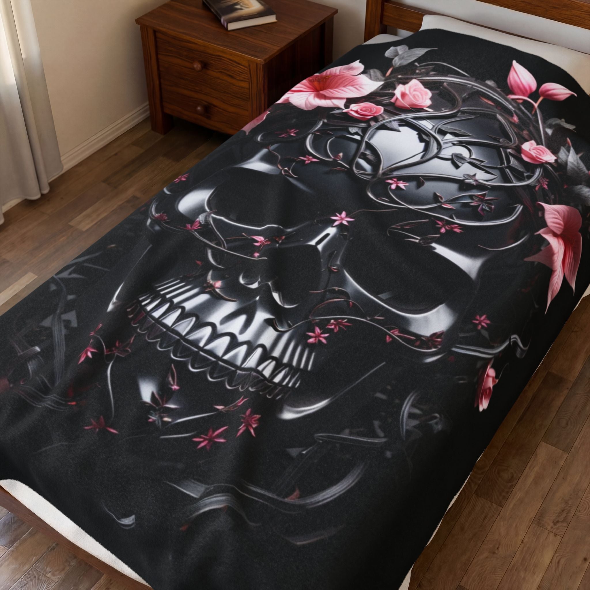 Black throw blanket with glossy black vine-wrapped skull surrounded by soft pink tropical blooms and scattered petals 
