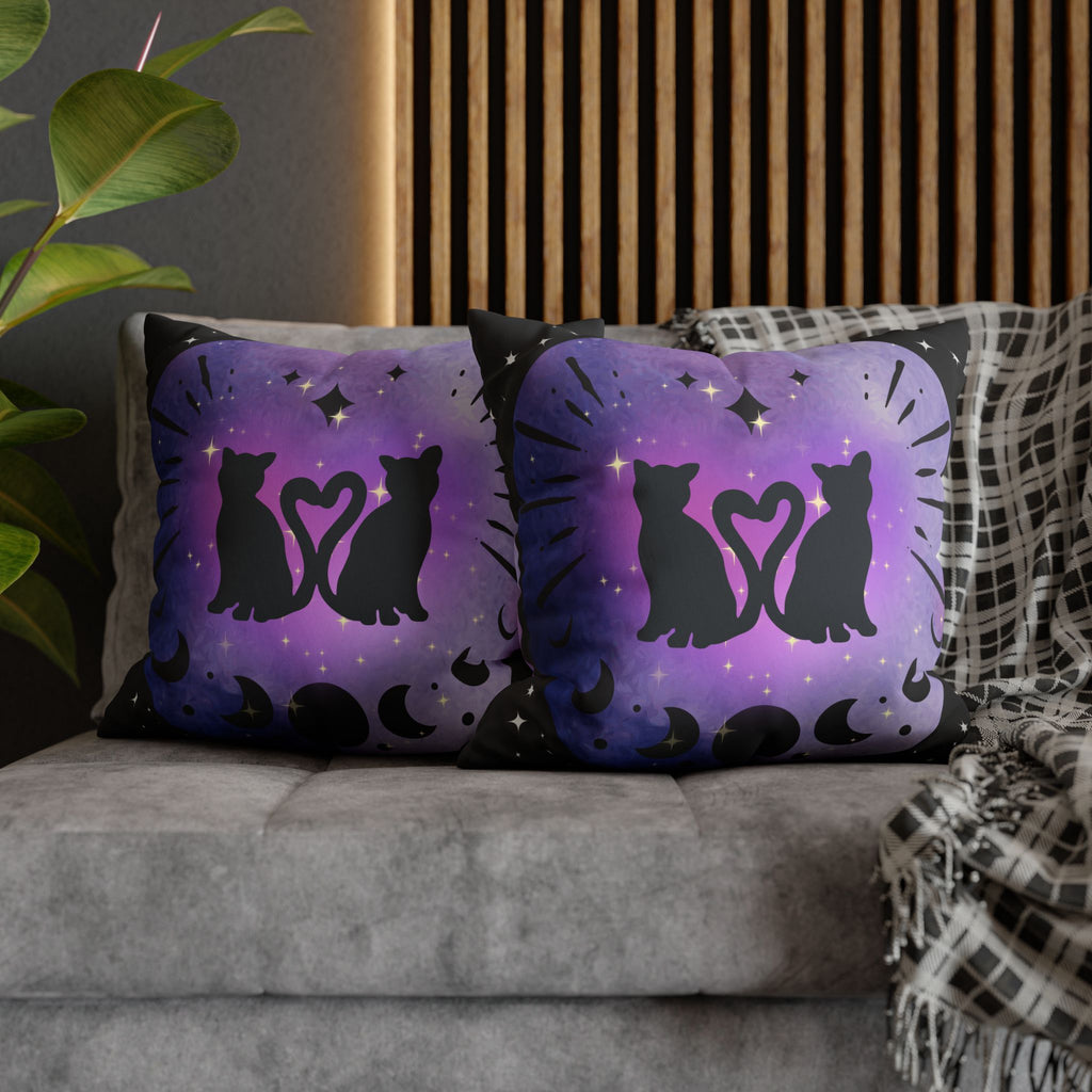 Two square throw pillows on a grey sofa featuring two black cat silhouettes facing each other with tails curled into a heart shape inside a soft purple to indigo watercolor vignette with moon phase sequence along the bottom and gold diamond stars on deep black