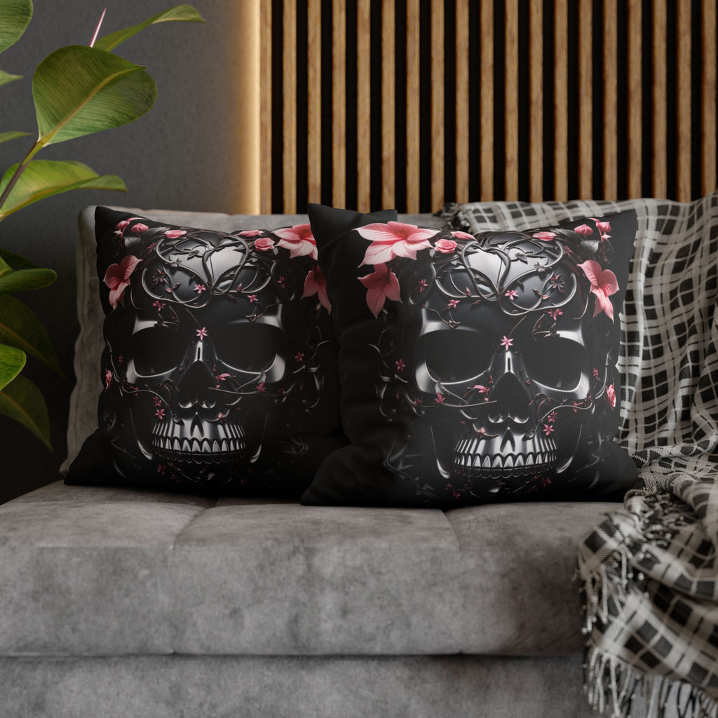 Two square throw pillows on a grey sofa featuring a large obsidian skull covered in intricate black iron vine and filigree work with soft pink roses and lilies blooming from the crown and eye sockets against a deep black background