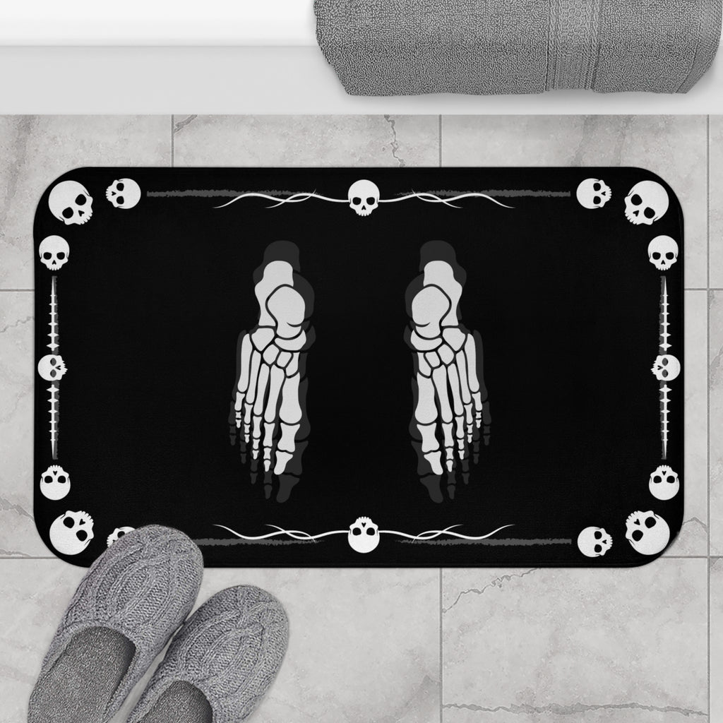 Gothic bath mat with two skeleton foot X-rays positioned in the center surrounded by a white skull icon and barbed wire border on a deep black background displayed on marble tile flooring