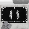 Gothic bath mat with two skeleton foot X-rays positioned in the center surrounded by a white skull icon and barbed wire border on a deep black background displayed on marble tile flooring