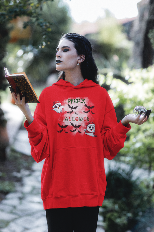 
Red hoodie with kawaii ghosts in Santa hats, bat swarm, and "I Prefer Halloween" text in red and green worn by a woman holding a book and crystal ball outdoors