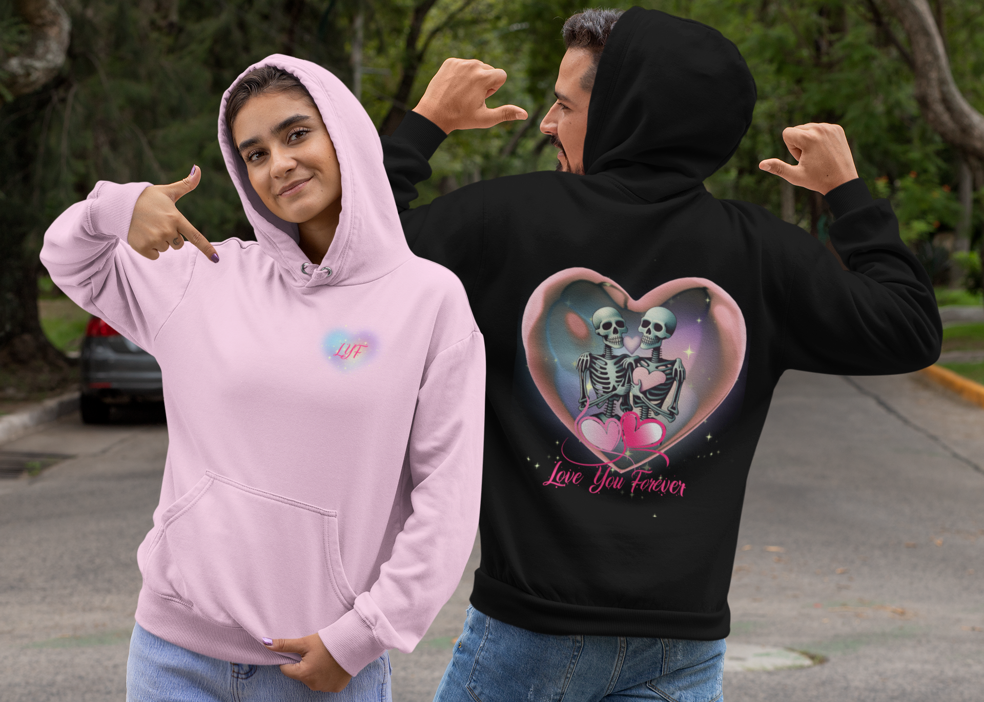 
Gothic Valentine's pullover hoodie shown in pink with "LYF" chest print and black with back print of two skeletons inside a glowing pink heart bubble with "Love You Forever" script worn by a couple outdoors