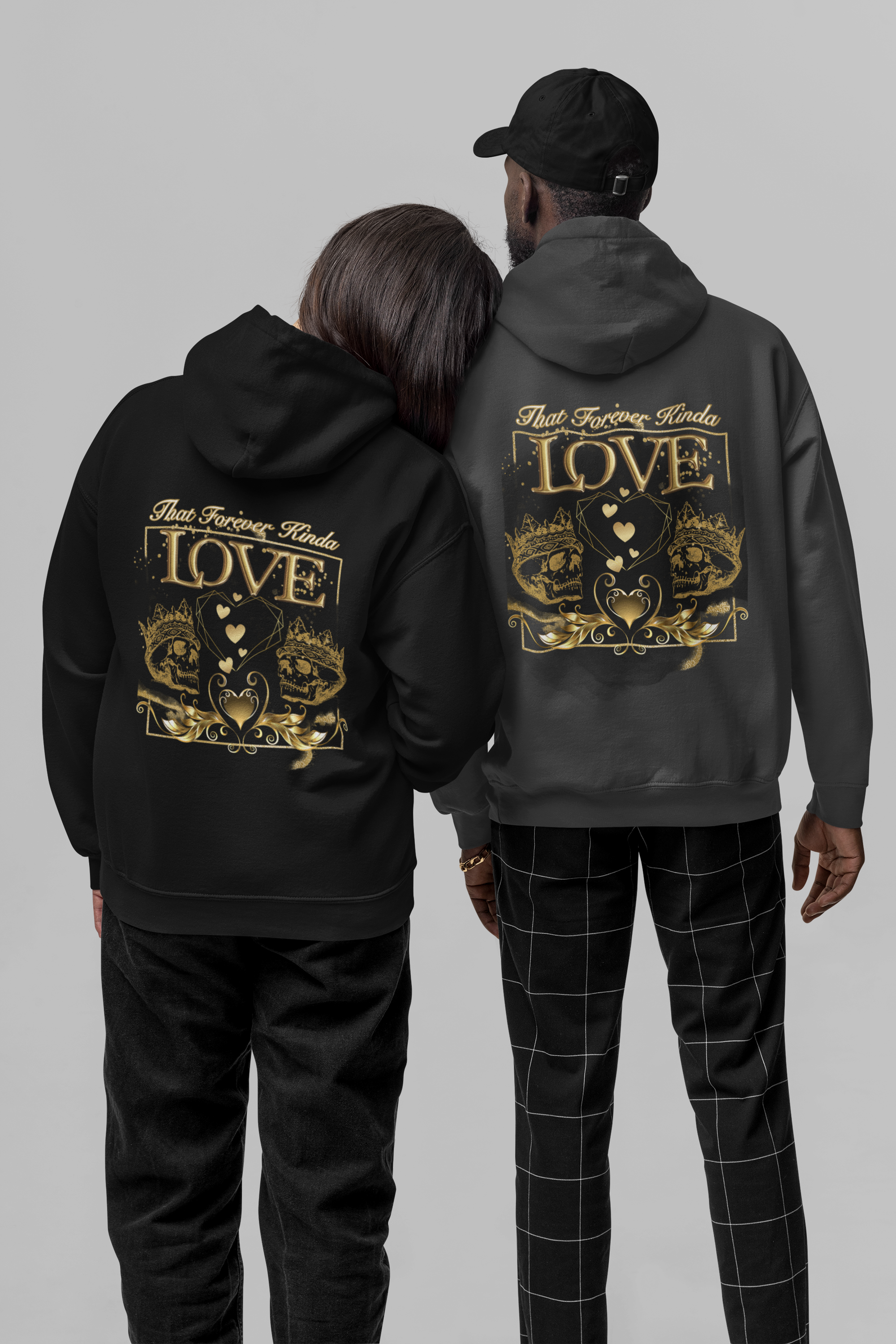 Gothic pullover hoodie back print showing two gold crowned skulls flanking a geometric heart with gold laurel scrollwork and "That Forever Kinda Love" script shown in black and dark heather worn by a couple