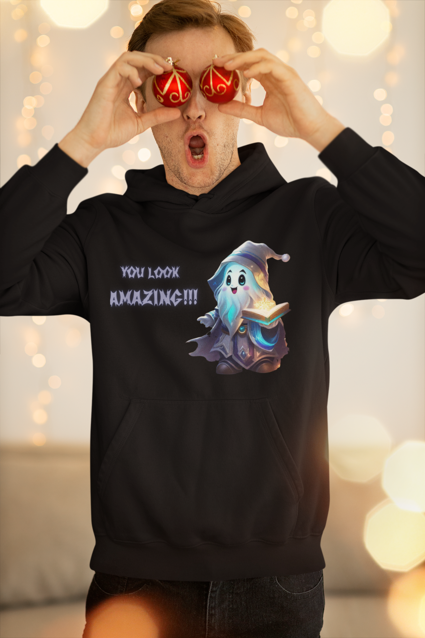 Black pullover hoodie with kawaii ghost in wizard armor and pointed hat holding a glowing spellbook with "You Look Amazing!!!" gothic lettering worn by a man holding Christmas ornaments over his eyes