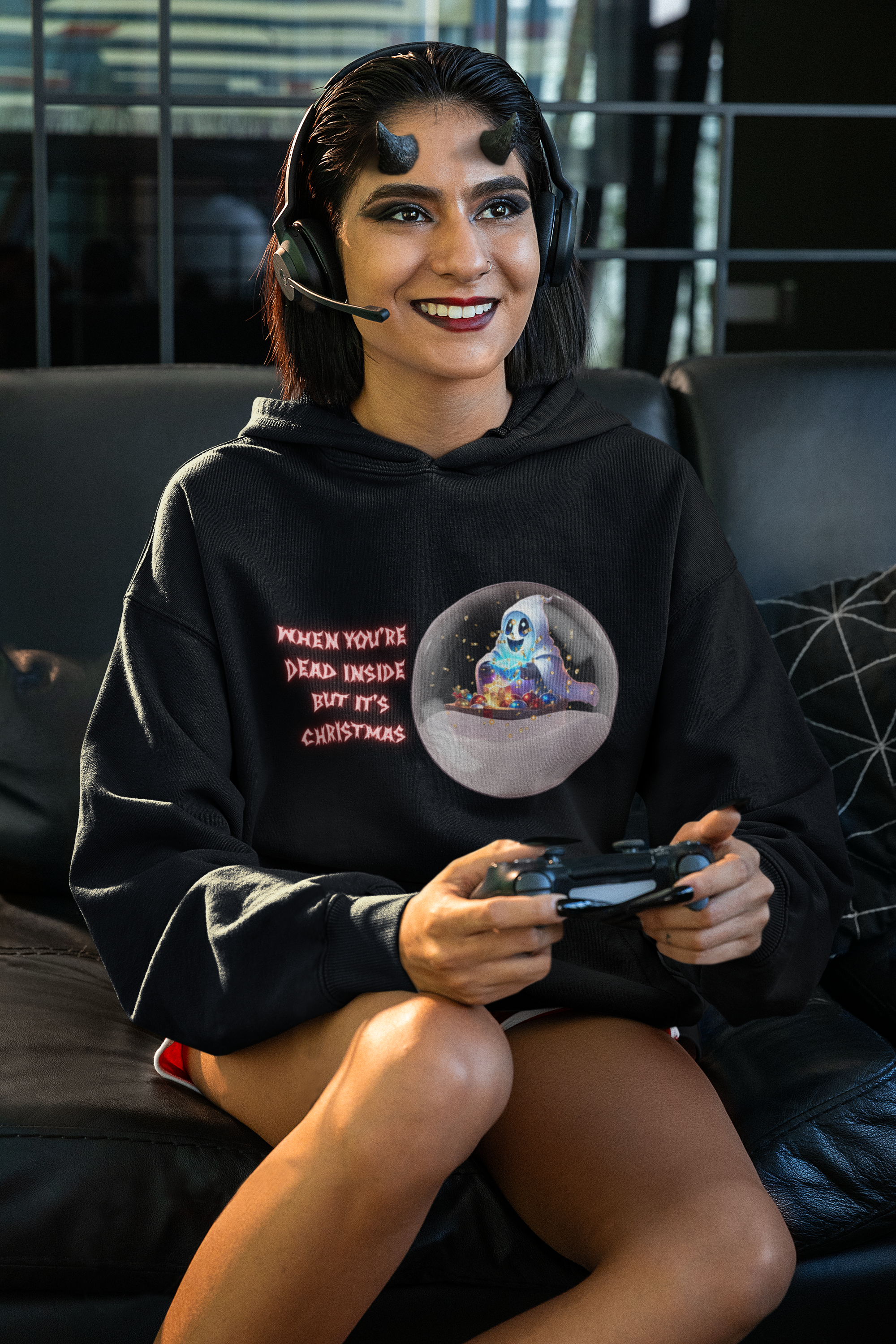 Black pullover hoodie with kawaii ghost inside a snow globe surrounded by colorful Christmas ornaments and "When You're Dead Inside But It's Christmas" in pink gothic lettering worn by a woman with devil horns playing video gamesSonnet 4.6