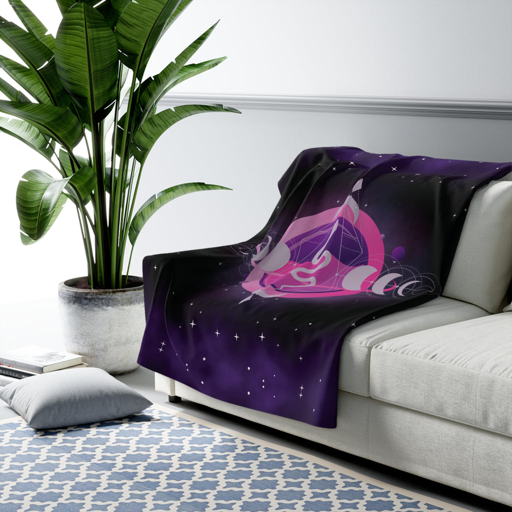 Deep purple and black throw blanket with glowing pink crystal orb containing a coiled snake flanked by moon phases and scattered stars draped over a sofa