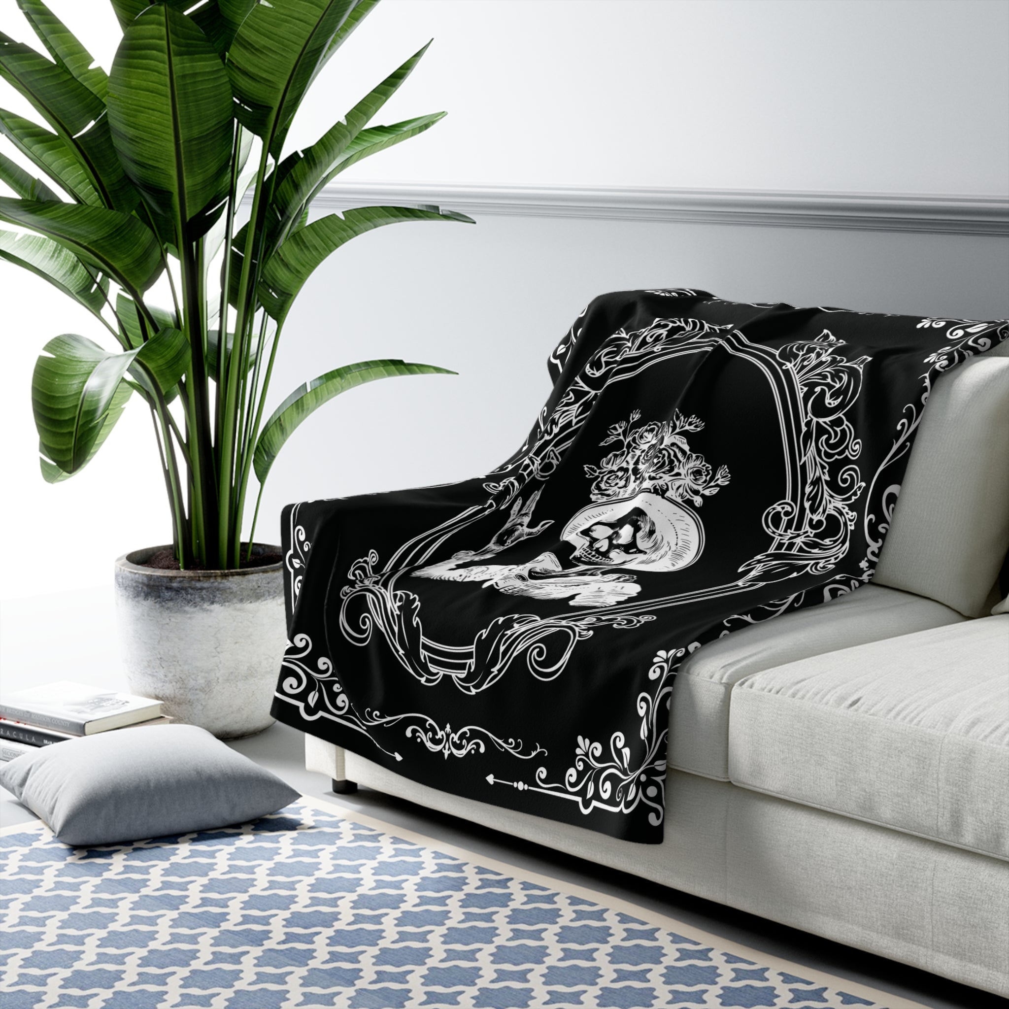 Gothic throw blanket with Victorian skeleton and ornate scrollwork border available in black and white or grey and black colorways draped over a sofa