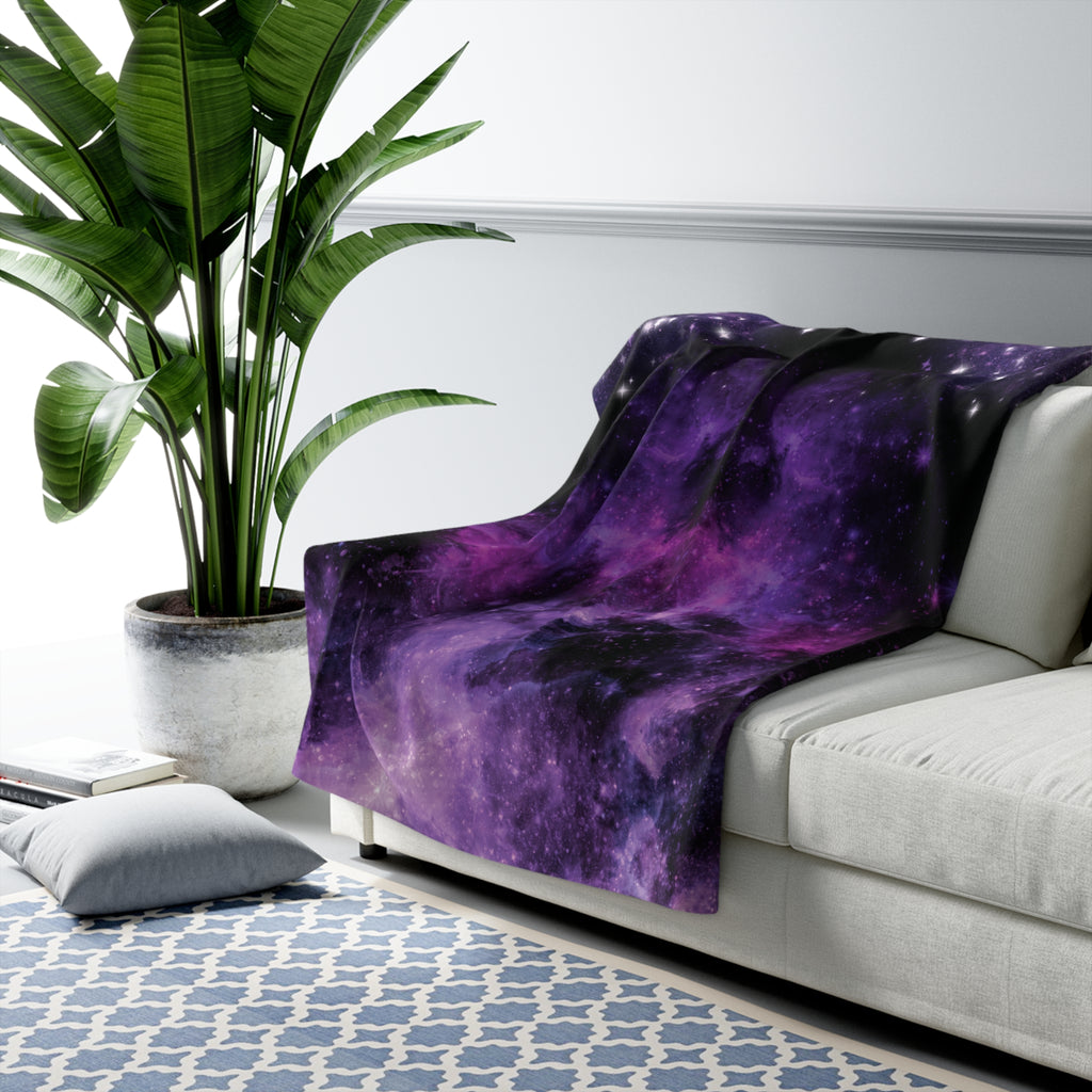 Deep purple and black galaxy nebula throw blanket with violet and amethyst tones and scattered star details draped over a sofa