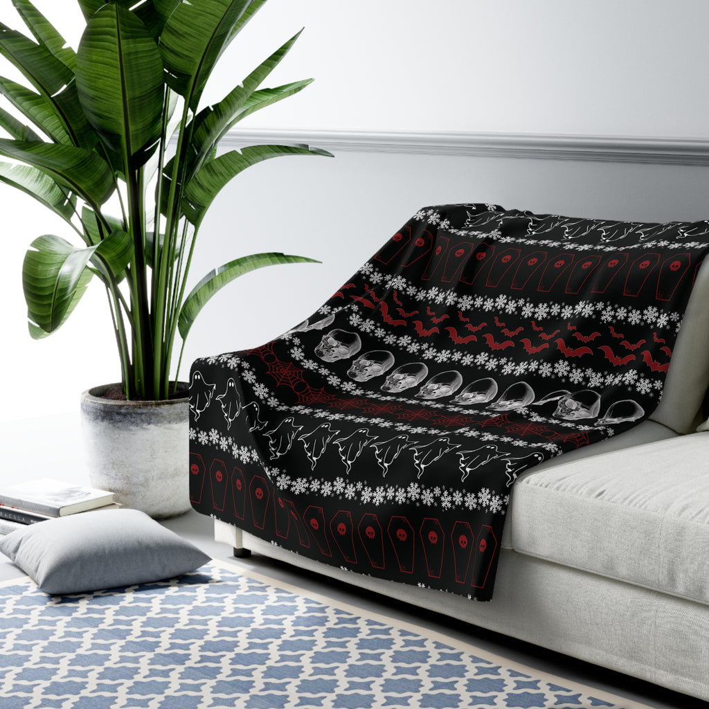 Black throw blanket with festive stripe pattern featuring ghosts, crystal skulls, red bats, coffins, spider webs, and white snowflakes draped over a sofa