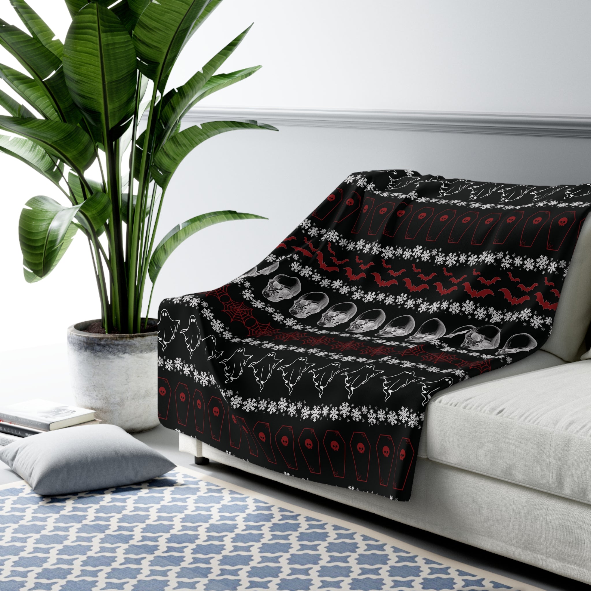 Black throw blanket with festive stripe pattern featuring ghosts, crystal skulls, red bats, coffins, spider webs, and white snowflakes draped over a sofa