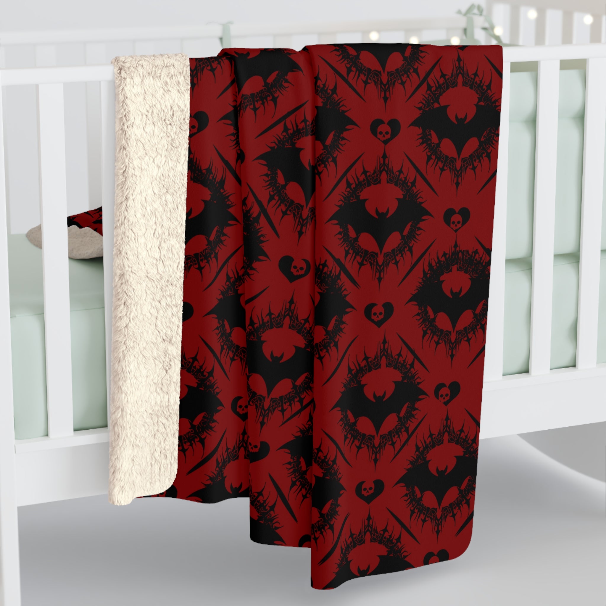Deep crimson red throw blanket with repeating gothic damask pattern of black bats and skull hearts displayed against a white crib background
