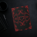 Gothic hardcover journal with crimson Victorian baroque scrollwork and centered heart design on a matte black background