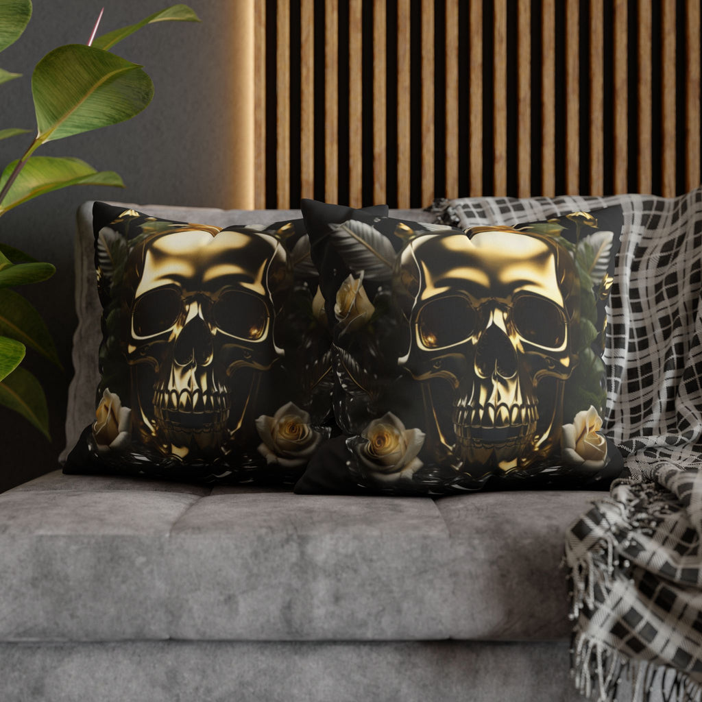 Two square throw pillows on a grey sofa featuring a large molten gold skull with deeply shadowed eye sockets surrounded by cream and ivory roses and dark botanical leaves against a deep black background