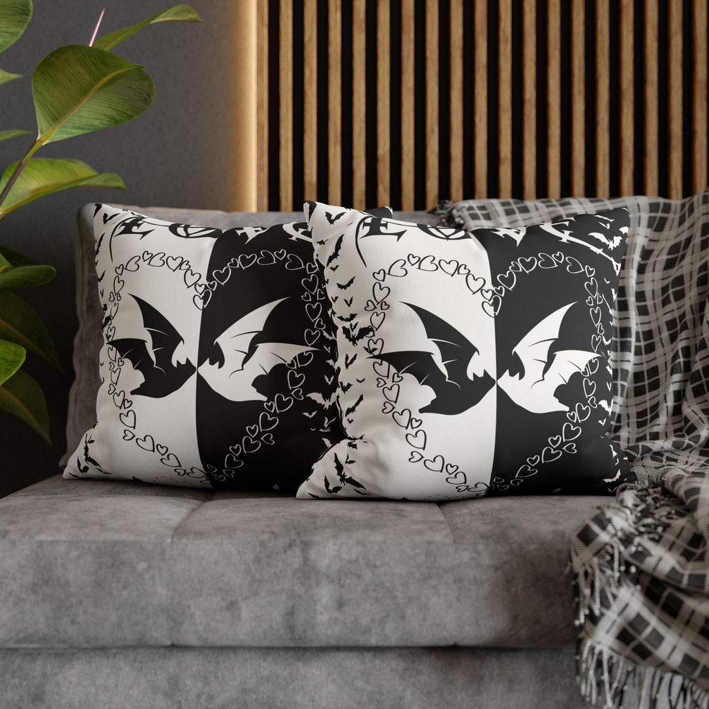 Two square throw pillows on a grey sofa featuring a bold split black and white design with large mirrored bat silhouettes surrounded by trailing chains of small hearts and scattered tiny bats on opposing halves