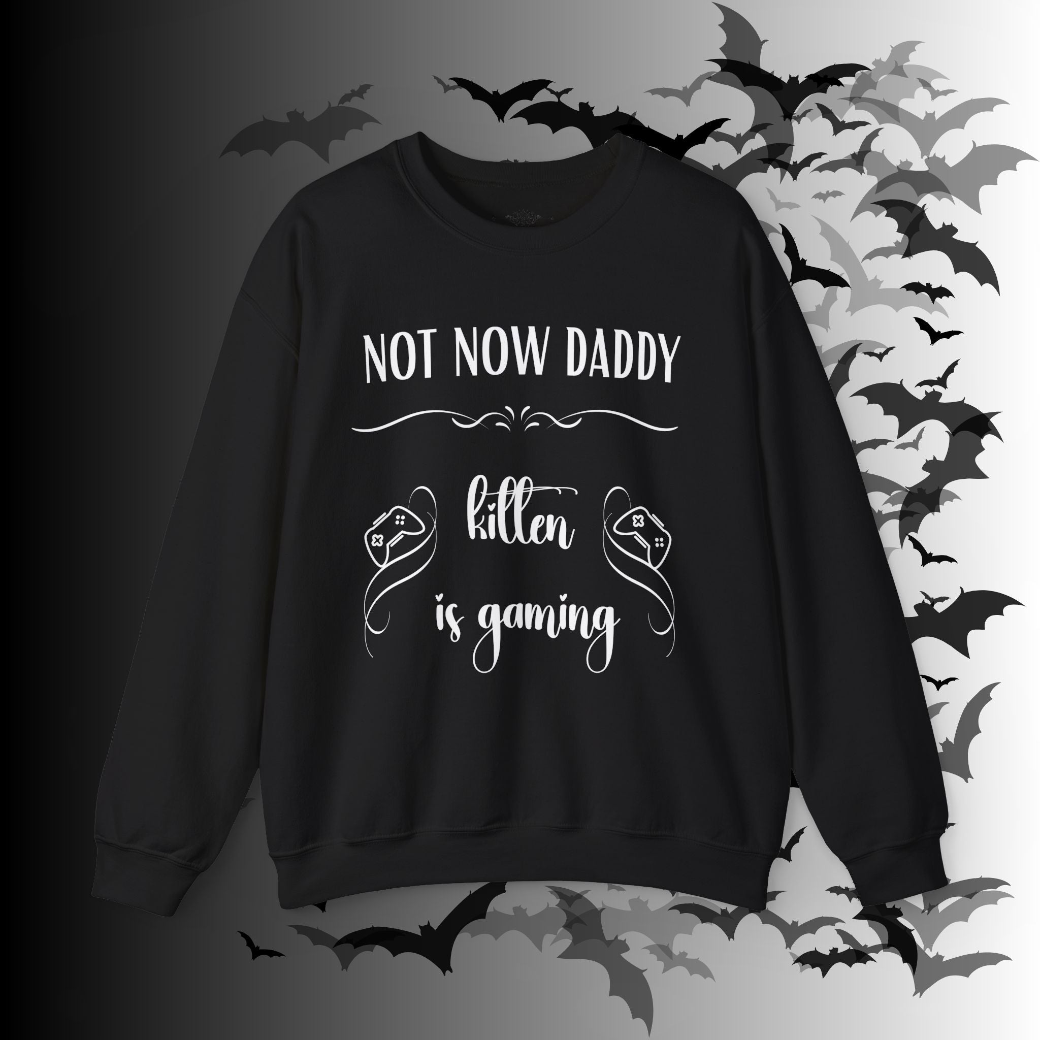 
Black crewneck sweatshirt with "Not Now Daddy" in bold block lettering and "kitten is gaming" in elegant script flanked by game controller graphics on a bat-filled background