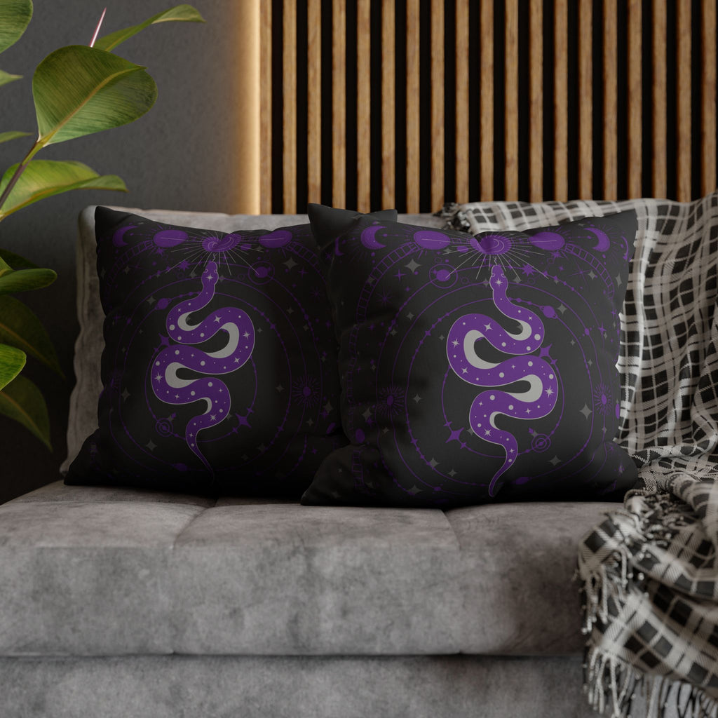 Two square throw pillows on a grey sofa featuring a coiling purple serpent with silver belly scales and star markings at the center of a circular celestial mandala with crescent moons, orbiting planets, radiant suns, and diamond stars in deep violet on black