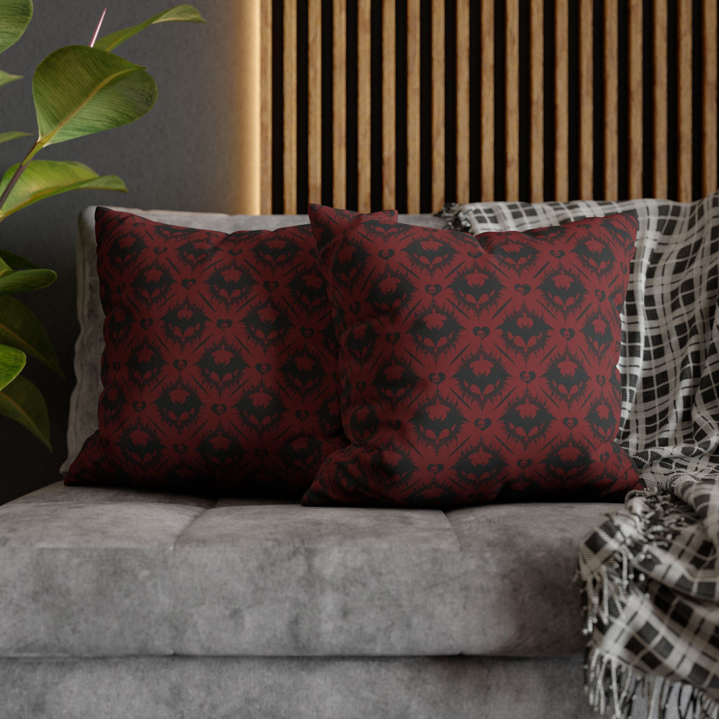 Two square throw pillows on a grey sofa featuring a repeating diamond grid pattern built from interlocking dark bat silhouettes with small heart centers in deep crimson red and near-black across the entire surface