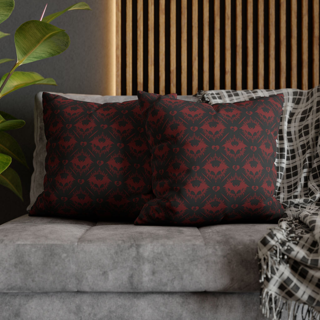 Two square throw pillows on a grey sofa featuring a repeating diamond grid of interlocking bat silhouettes with small heart centers rendered in midnight black with deep crimson accent tones across the entire surface