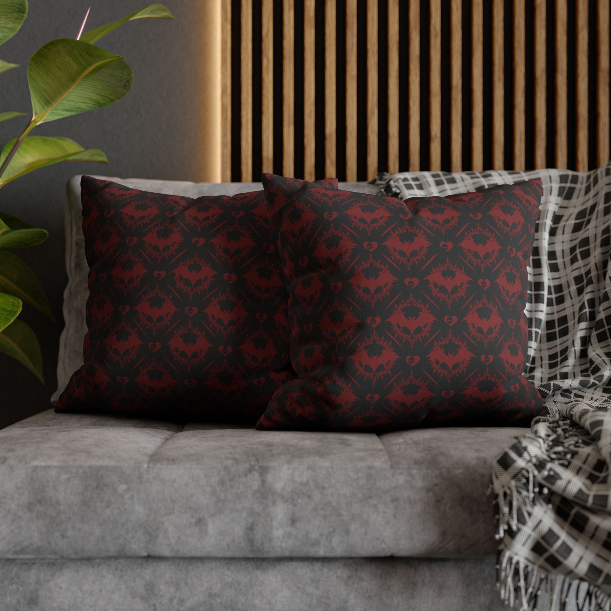 Two square throw pillows on a grey sofa featuring a repeating diamond grid of interlocking bat silhouettes with small heart centers rendered in midnight black with deep crimson accent tones across the entire surface