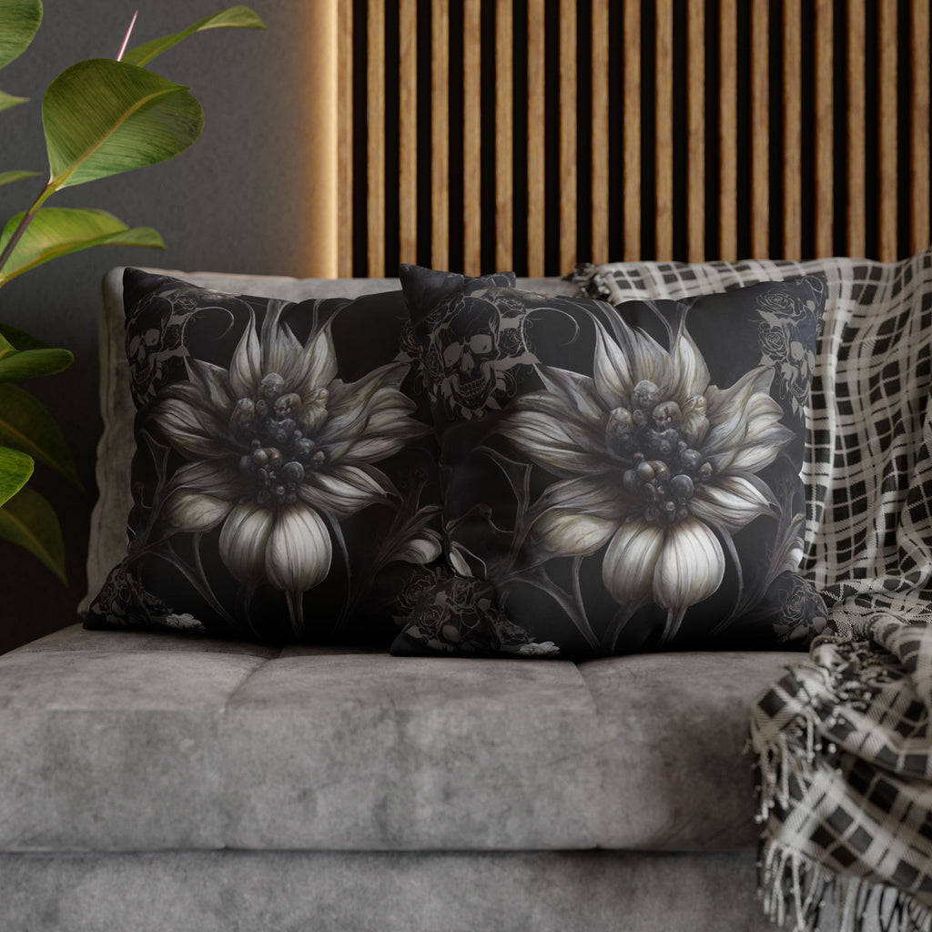 Two square throw pillows on a grey sofa featuring large ghostly white sunflowers with skull cluster centers in monochromatic grey and white with smaller skull and rose motifs drifting through the dark background connected by trailing vines against deep black