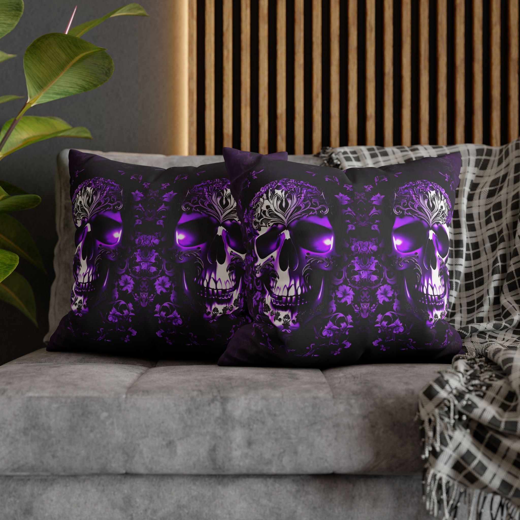 Two square throw pillows on a grey sofa featuring a large ornate skull with glowing violet eyes and baroque filigree crown detailing against a deep purple damask floral pattern on black background