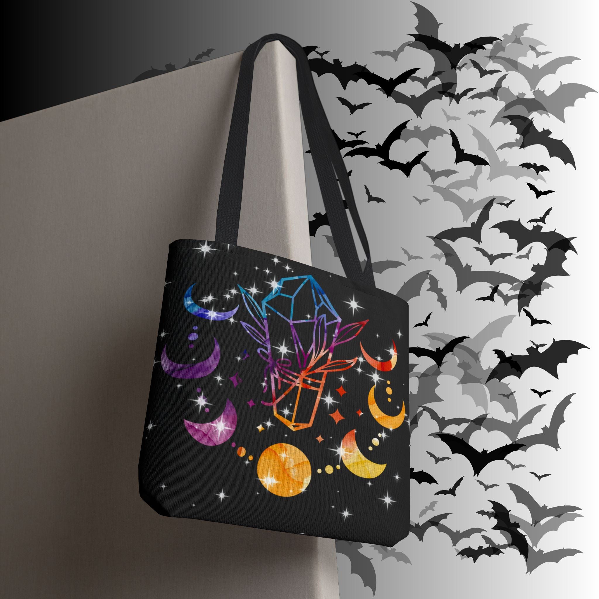 Black polyester tote bag with rainbow geometric crystals, purple and amber crescent moons, golden orbs, and four-pointed star bursts on a deep black background